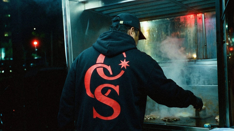 Sudadera con capucha negra con el monograma CCS de Caracas Merch, vista de espaldas de noche