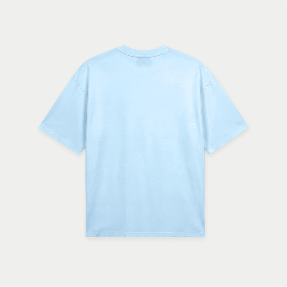 Light blue oversized t-shirt back view with collage-style graphic featuring paint palette, brushes, and vintage classroom images with “Caracas” text – Caracas Merch