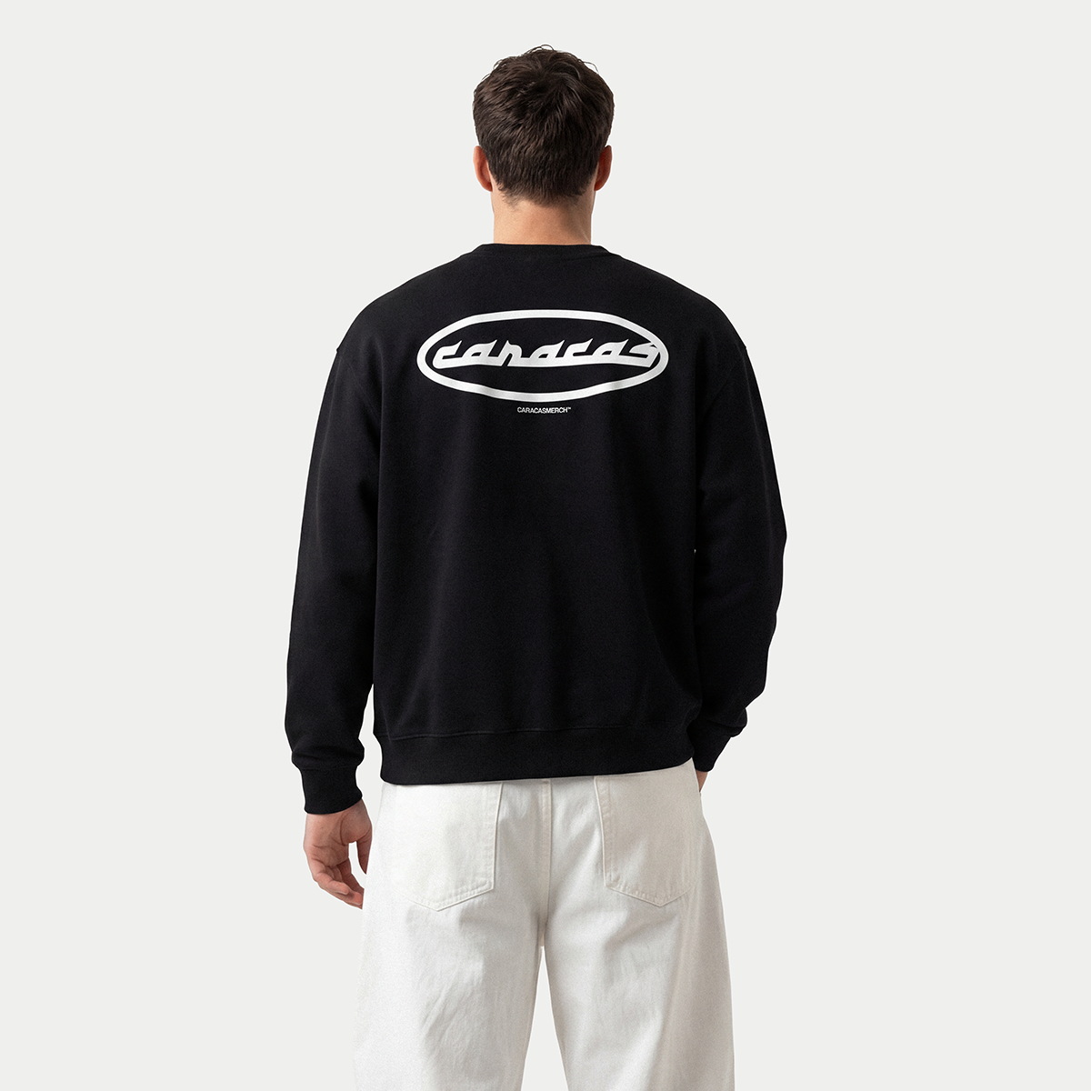 Back view of black Caracas Merch crewneck worn by male model
