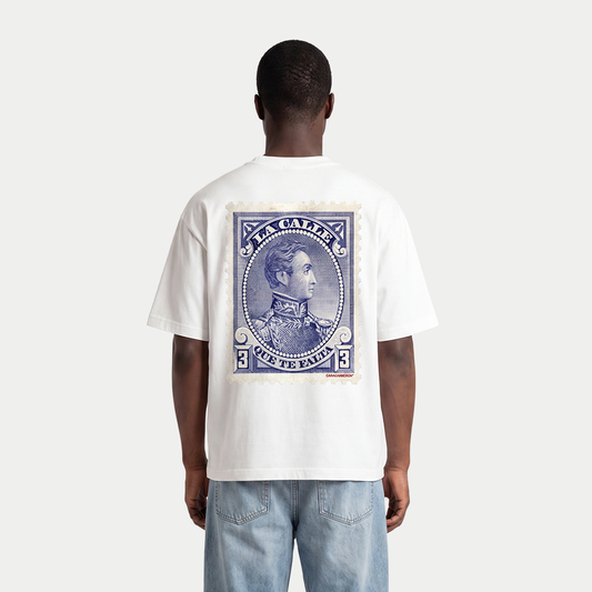Model wearing white oversized t-shirt back view with large vintage blue postage stamp graphic featuring a classic portrait and “Te falta” text – Caracas Merch
