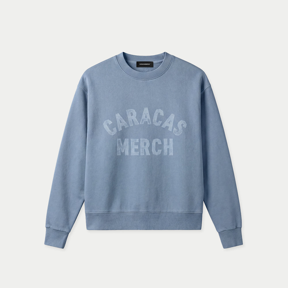 Blauer Oversized Vintage-Wash-Crewneck von Caracas Merch mit gebogenem „Caracas Merch“-Logo auf der Brust, Vorderansicht