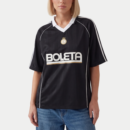 Female model wearing black soccer-style jersey front view with striped texture, V-neck collar, and bold “BOLETA” graphic across the chest – Caracas Merch
