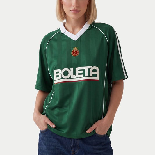 Female model wearing green soccer-style jersey front view with striped texture, V-neck collar, and bold “BOLETA” graphic across the chest – Caracas Merch