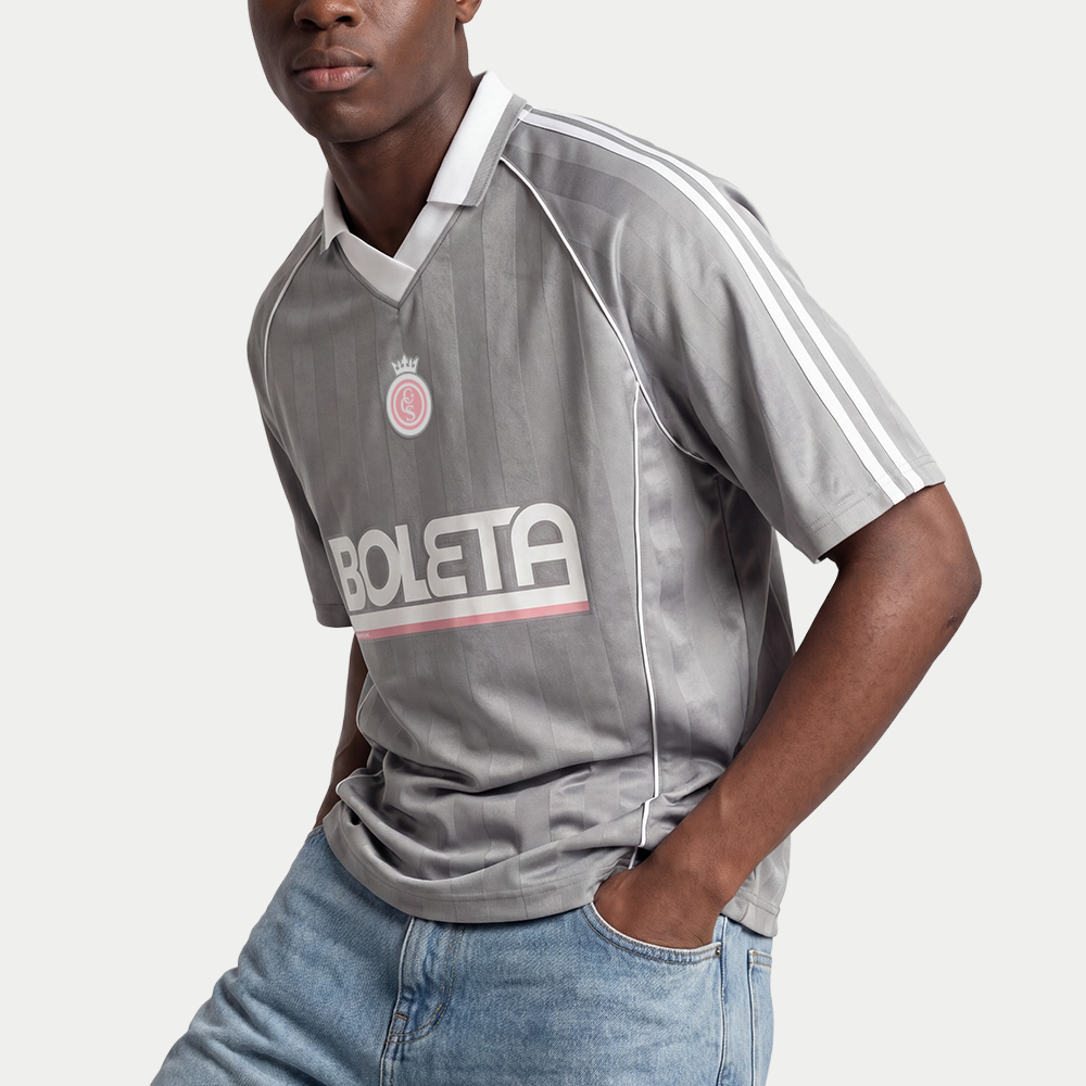 Male model wearing grey soccer-style jersey front view with striped texture, V-neck collar, and bold “BOLETA” graphic across the chest – Caracas Merch