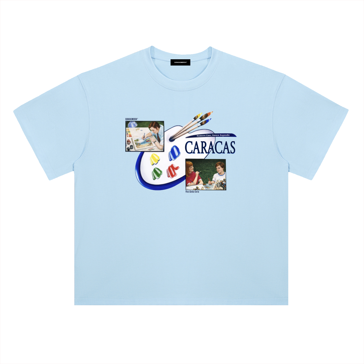 Light blue oversized t-shirt front view with collage-style graphic featuring paint palette, brushes, and vintage classroom images with “Caracas” text – Caracas Merch