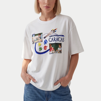 Female model wearing oversized t-shirt front view with collage-style graphic featuring paint palette, brushes, and vintage classroom images with “Caracas” text – Caracas Merch