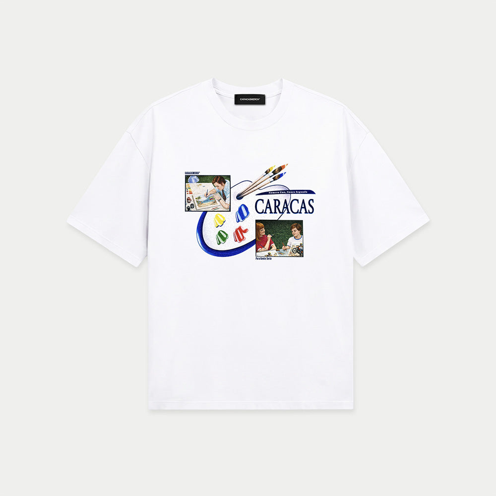 White oversized t-shirt front view with collage-style graphic featuring paint palette, brushes, and vintage classroom images with “Caracas” text – Caracas Merch