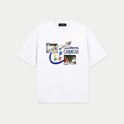 White oversized t-shirt front view with collage-style graphic featuring paint palette, brushes, and vintage classroom images with “Caracas” text – Caracas Merch