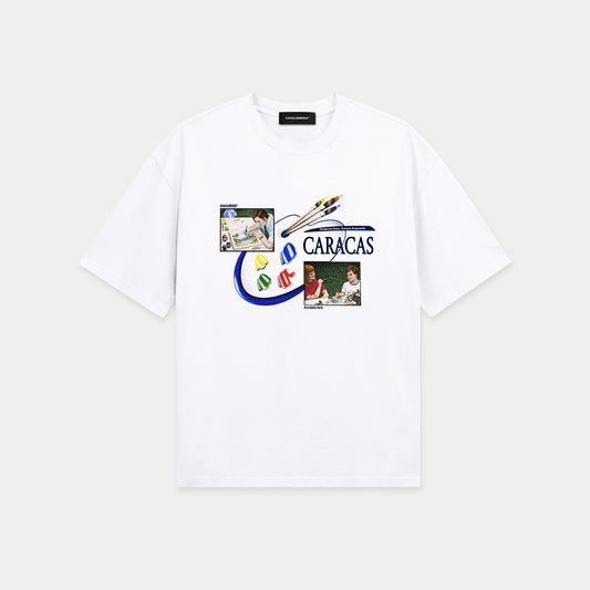 White oversized t-shirt front view with collage-style graphic featuring paint palette, brushes, and vintage classroom images with “Caracas” text – Caracas Merch