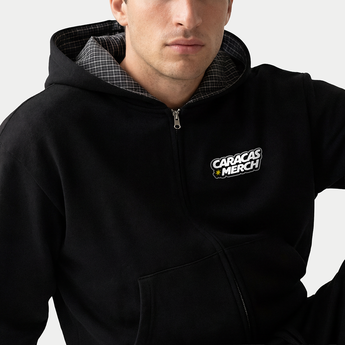 Close-up of black zip-up hoodie with Caracas Merch logo and plaid hood lining