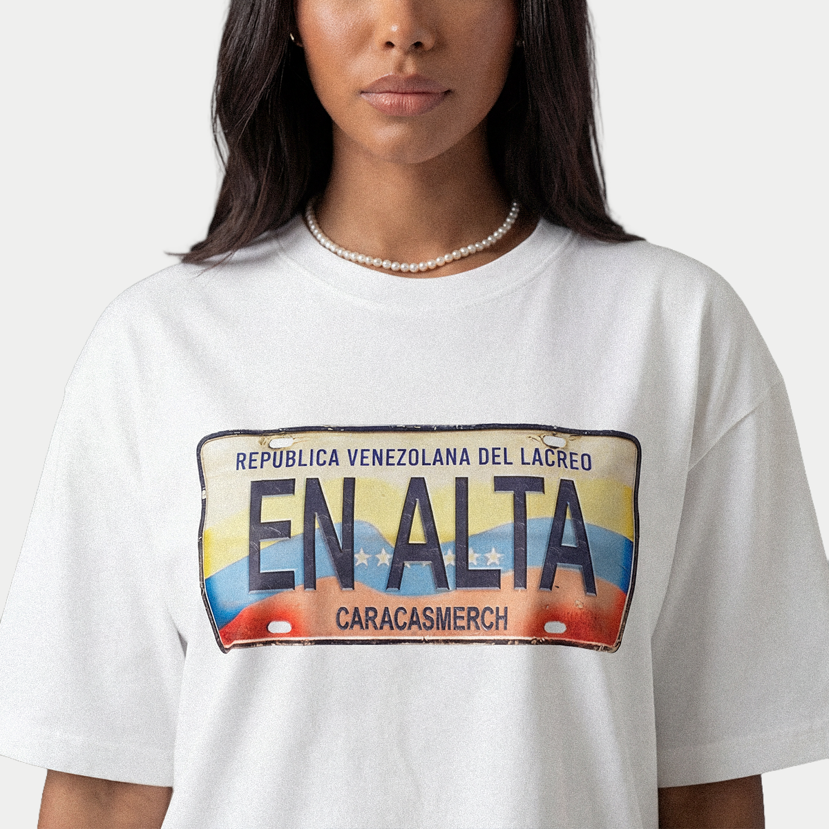 Close-up of En Alta license plate graphic on white Caracas Merch t-shirt