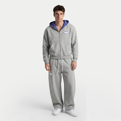Male model wearing gray zip-up hoodie and sweatpants with blue hood lining by Caracas Merch
