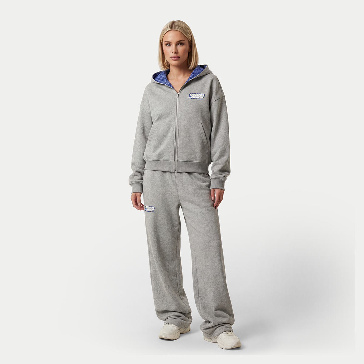 Female model wearing gray zip-up hoodie and sweatpants with blue hood lining by Caracas Merch