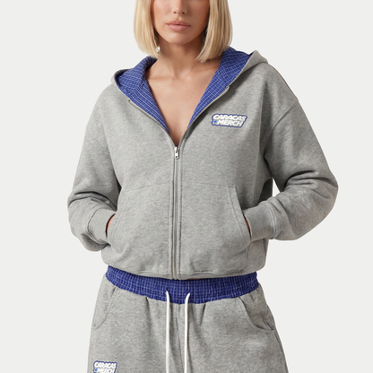 Close-up of women’s gray zip-up hoodie featuring blue hood lining and embroidered Caracas Merch logo
