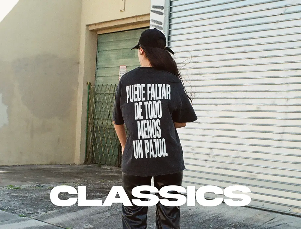 Persona de espaldas con la camiseta negra «Puede faltar de todo menos un pajuo» de Caracas Merch, banner de la colección Classics