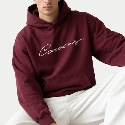 Model wearing burgundy Caracas script hoodie by Caracas Merch