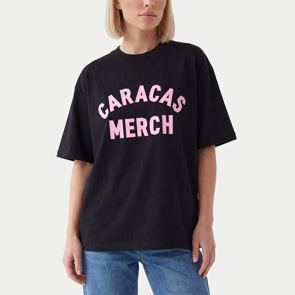Model wearing a black oversized Caracas Merch t-shirt with arched pink logo at front