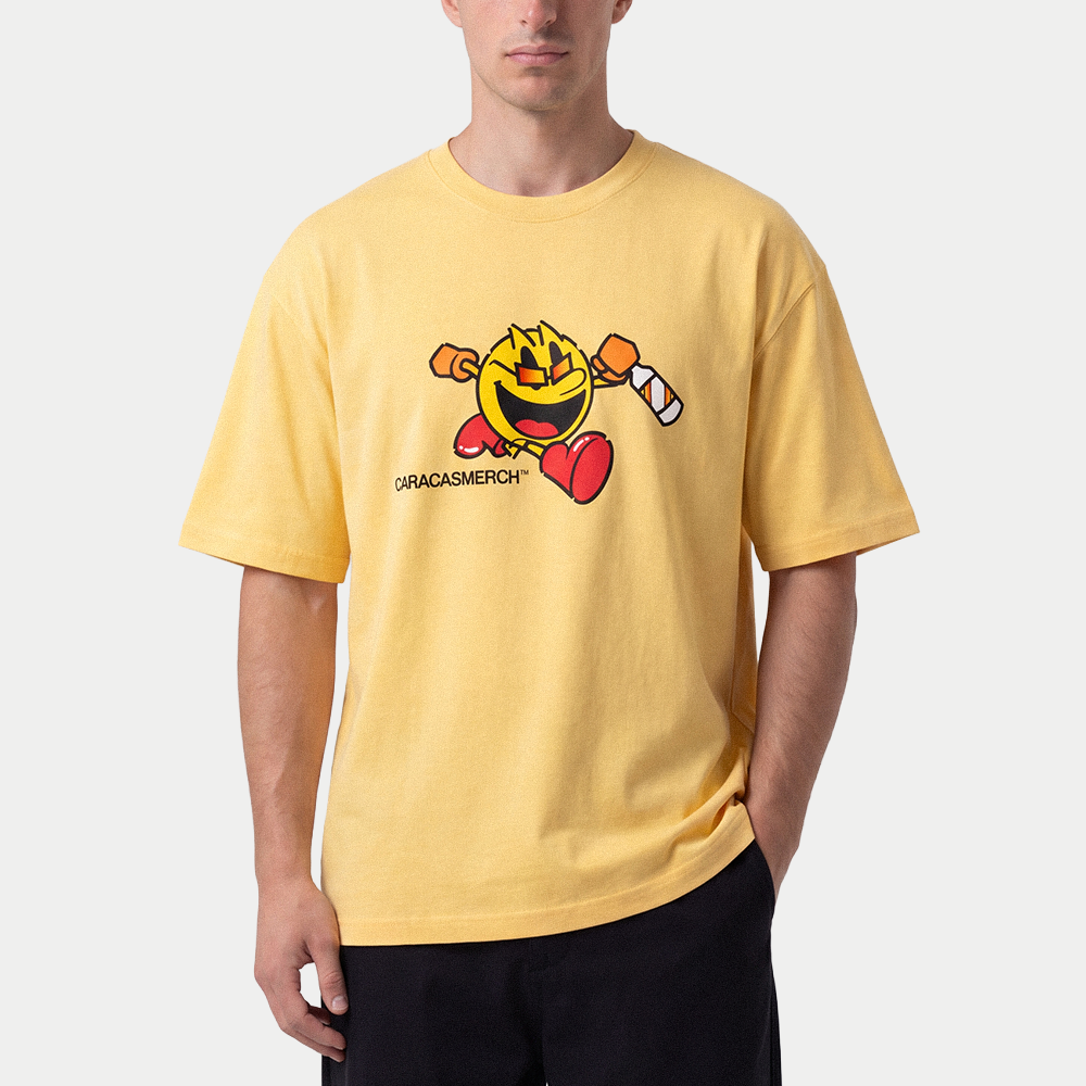 Male model wearing yellow oversized t-shirt front view with cartoon running character graphic holding a bottle and Caracas Merch logo underneath