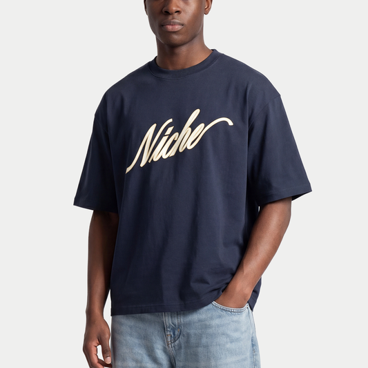 Male model wearing navy blue oversized boxy t-shirt front view with elegant “Niche” script logo in white centered on the chest – Caracas Merch