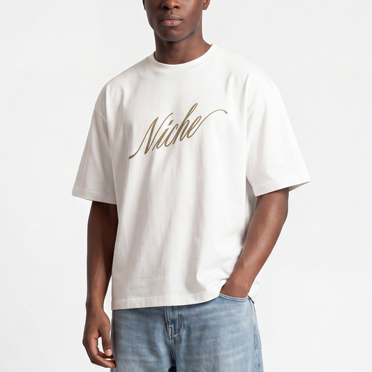 Male model wearing white boxy oversized t-shirt front view with elegant “Niche” script logo in gold centered on the chest – Caracas Merch