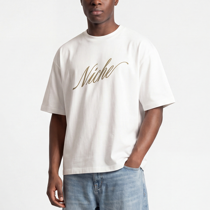 Male model wearing white boxy oversized t-shirt front view with elegant “Niche” script logo in gold centered on the chest – Caracas Merch
