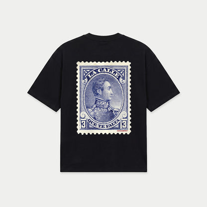 Black oversized t-shirt back view with large vintage blue postage stamp graphic featuring a classic portrait and “la calle que te falta” text – Caracas Merch