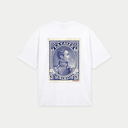 White oversized t-shirt back view with large vintage blue postage stamp graphic featuring a classic portrait and “la calle que te falta” text – Caracas Merch