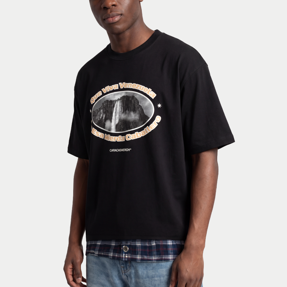 Model wearing Black boxy t-shirt front view with oval graphic featuring Angel Falls image and “Que viva Venezuela en esa mierda caballero” text – Caracas Merch