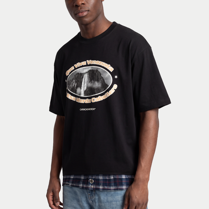 Model wearing Black boxy t-shirt front view with oval graphic featuring Angel Falls image and “Que viva Venezuela en esa mierda caballero” text – Caracas Merch