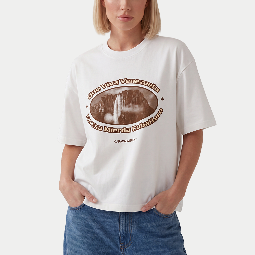 Female model wearing white boxy t-shirt front view with oval graphic featuring Angel Falls image and “Que viva Venezuela en esa mierda caballero” text – Caracas Merch