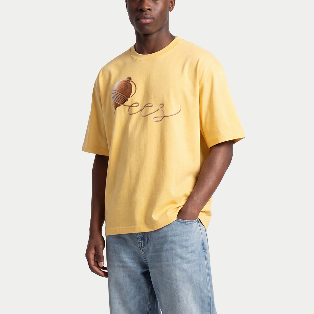 Male model wearing yellow oversized t-shirt front view with wooden spinning top graphic forming “ccs” in rope-style lettering – Caracas Merch